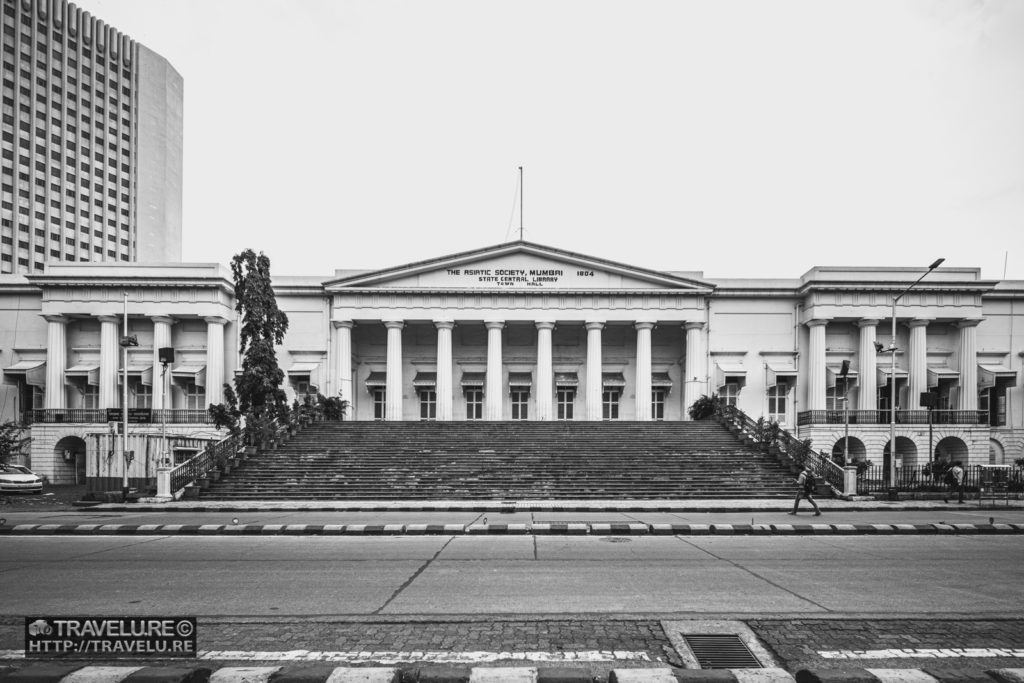 The Asiatic Society of Mumbai (or colloquially, the Asiatic Library) building was completed in 1833 and holds over 100,000 books (15,000 of these, classified as rare), 3,000 manuscripts in Persian, Sanskrit, and Prakrit, almost 12,000 rare coins (including a few gold coins from different eras), and 1,300 maps. Many popular scenes from the movies have been shot on its imposing staircase. And its neoclassical architecture with an empty road in front makes this sprawling building look unified and compact.