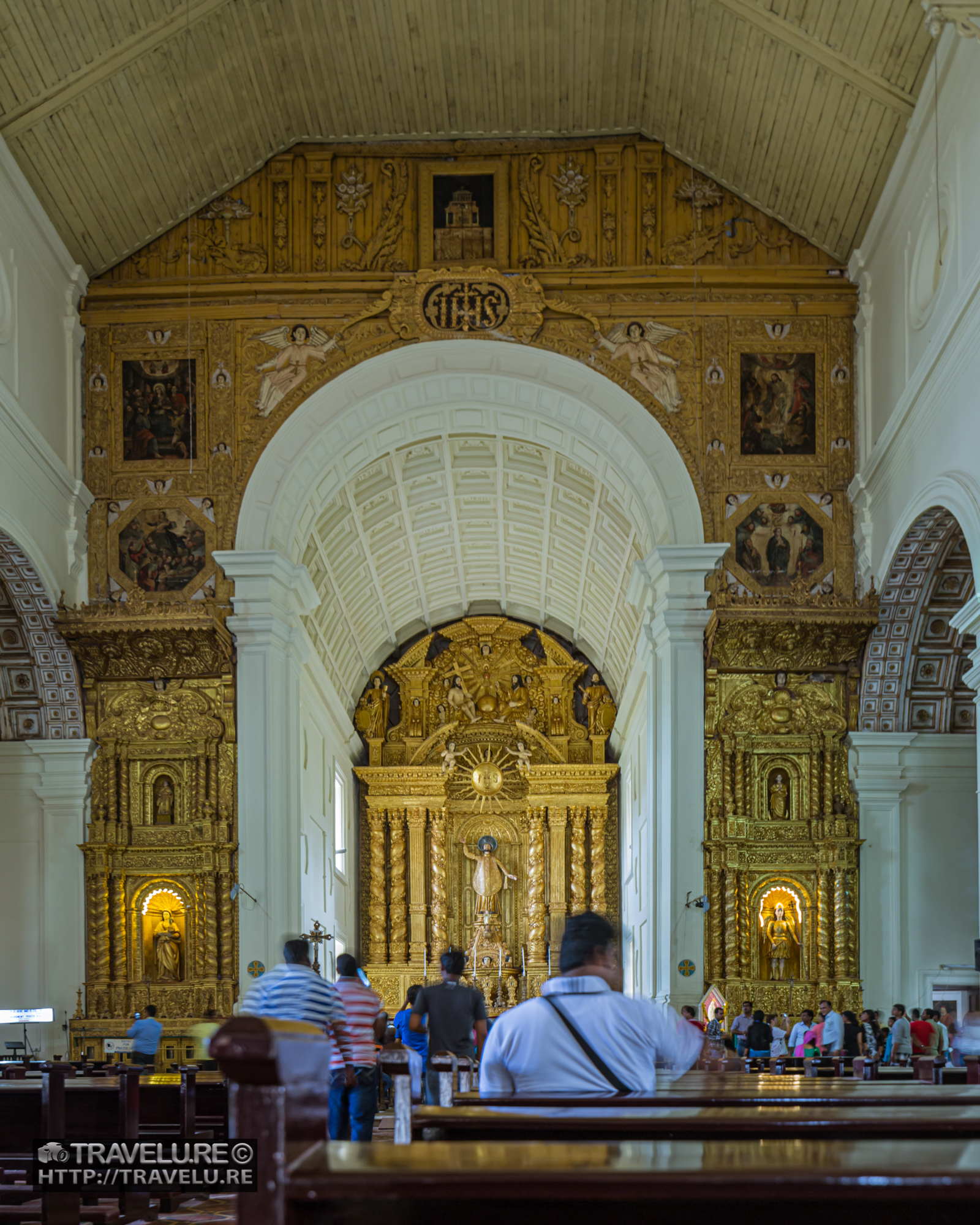 Interior of the Basilica of Bom Jesus, Old Goa — gilded Baroque altar and nave, visitors in silhouette, natural light, Goa, India.