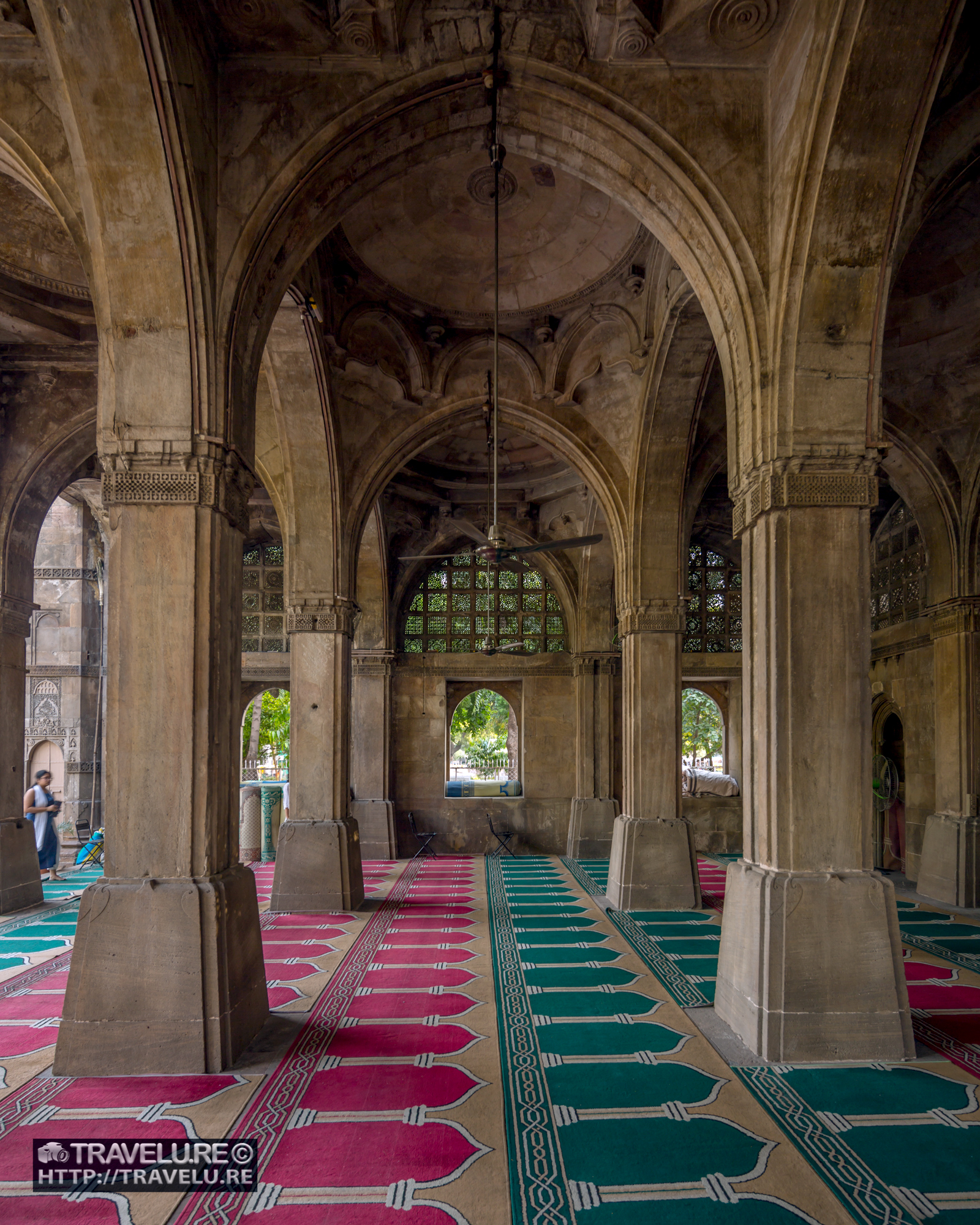 Interior of Sidi Saiyyed Mosque, Ahmedabad — pointed stone arches, jali screens backlit in upper windows, prayer carpets on the floor, Gujarat, India.