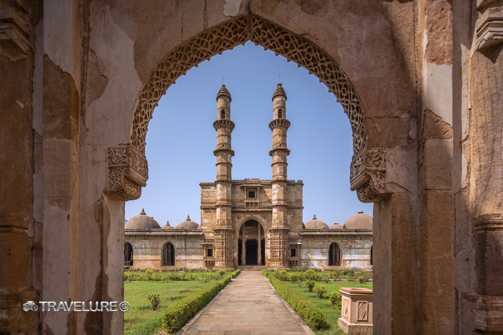 Kevda Masjid at Champaner-Pavagadh Archaeological Park, framed through a carved stone lattice arch, twin minarets centred, Gujarat, India — UNESCO World Heritage Site.