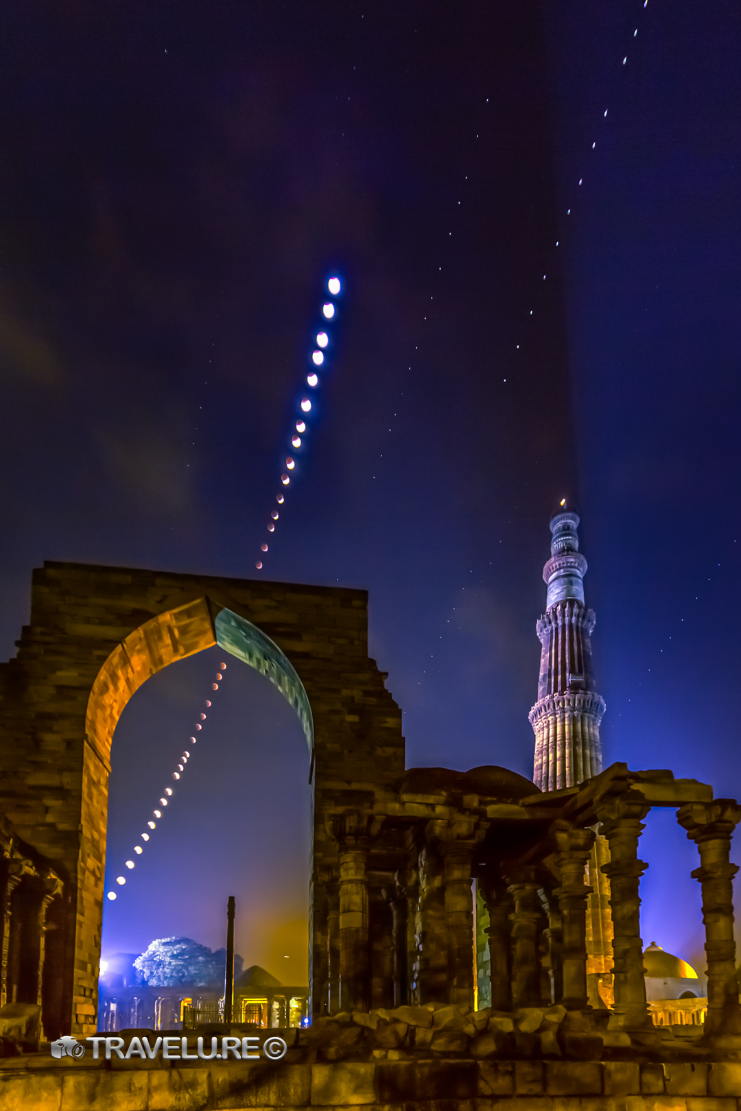 Total lunar eclipse composite at Qutub Minar — 36-frame arc of moon phases through Quwwat-ul-Islam mosque arch, blood moon at totality, Qutub Minar lit at right, Delhi. ASI-permitted night shoot.
